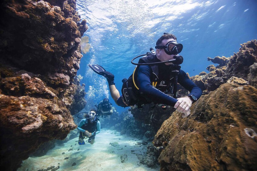 Two scuba divers exploring a coral reef with rocky formations. 1