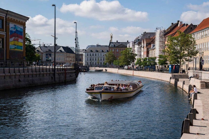 A boat on a canal with buildings and a bridge in the background. 1