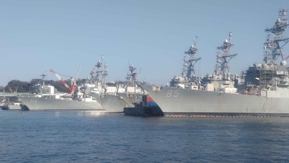 Three large naval ships docked at a port with cranes and other industrial equipment in the background. 5