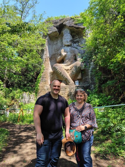 A man and a woman standing in front of a large rock with a carved statue. 4
