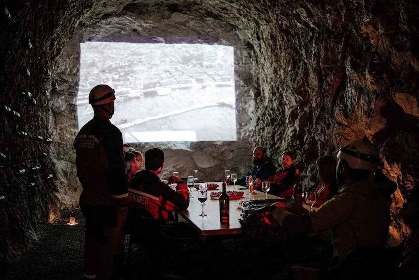 A group of people in a cave with a table and wine glasses. 1