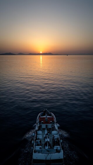 A boat moving towards a sunset over calm water with distant mountains. 5
