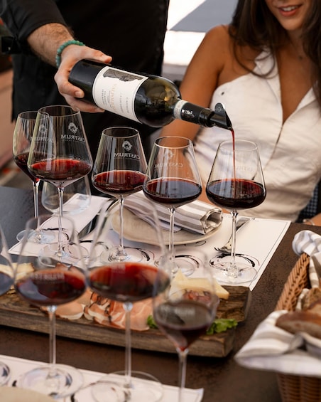 A person pouring red wine into glasses on a table with a cheese board. 5