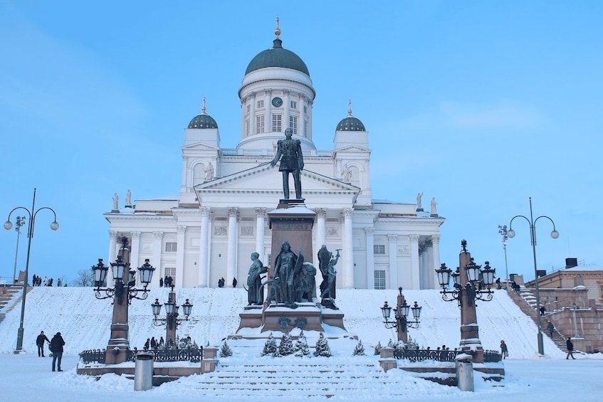 A snow-covered statue in front of a large white building with domes. 4