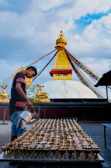 A person pouring water onto a large number of lit oil lamps arranged in rows. 4