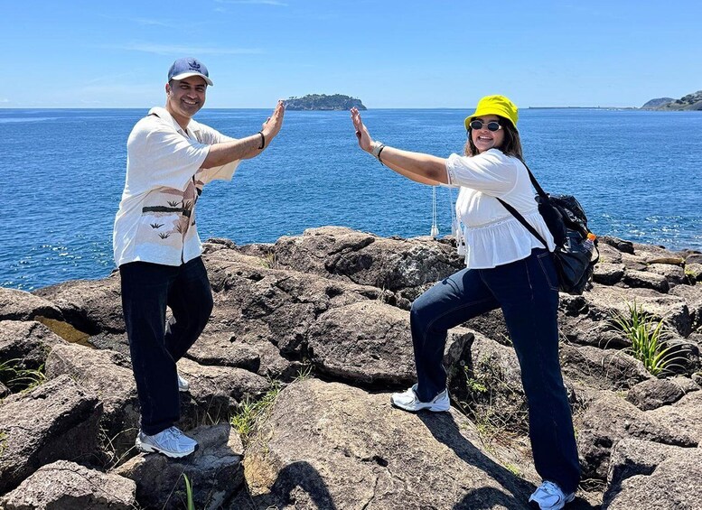 Two people posing on rocky terrain by the sea with a distant island in the background. 2