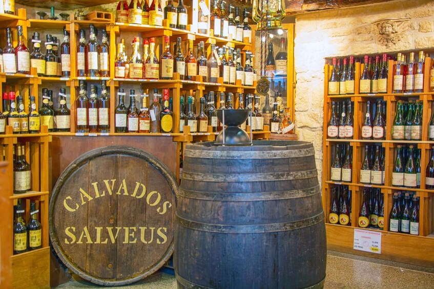 A wine cellar with wooden shelves stocked with various bottles of wine. A large wooden barrel with the inscription 'CALVADOS SALVEUS' is prominently displayed in the foreground. 5