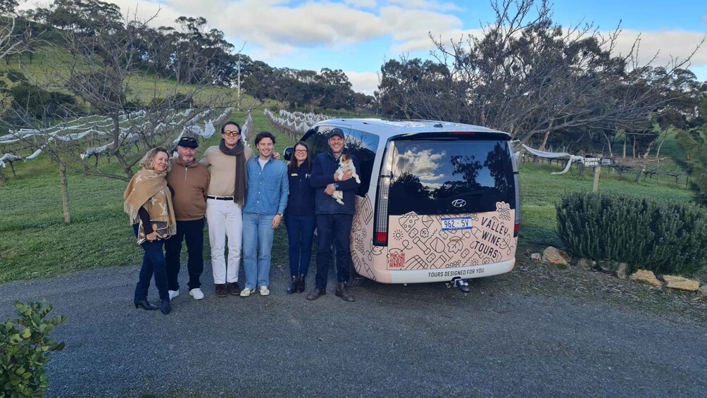 A group of people standing beside a vehicle with a wine tour advertisement on the back. 1