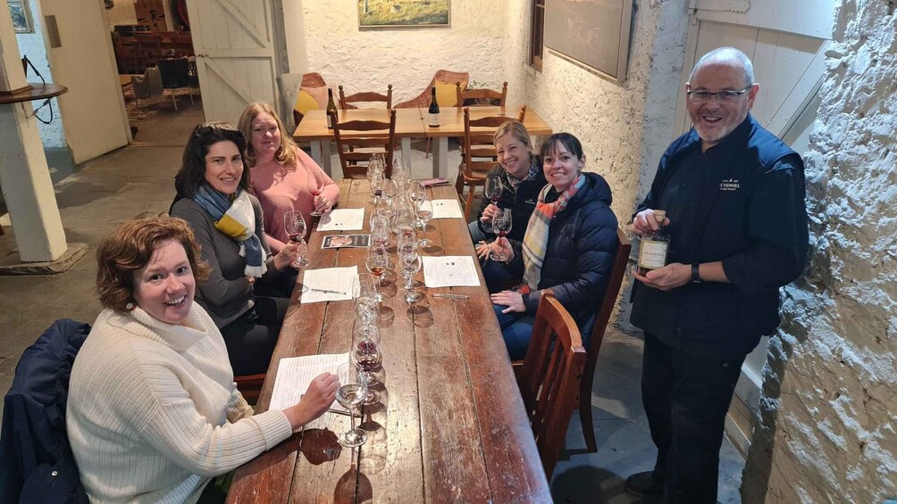 A group of people seated around a wooden table with wine glasses and menus, in a rustic interior with exposed brick walls. 2