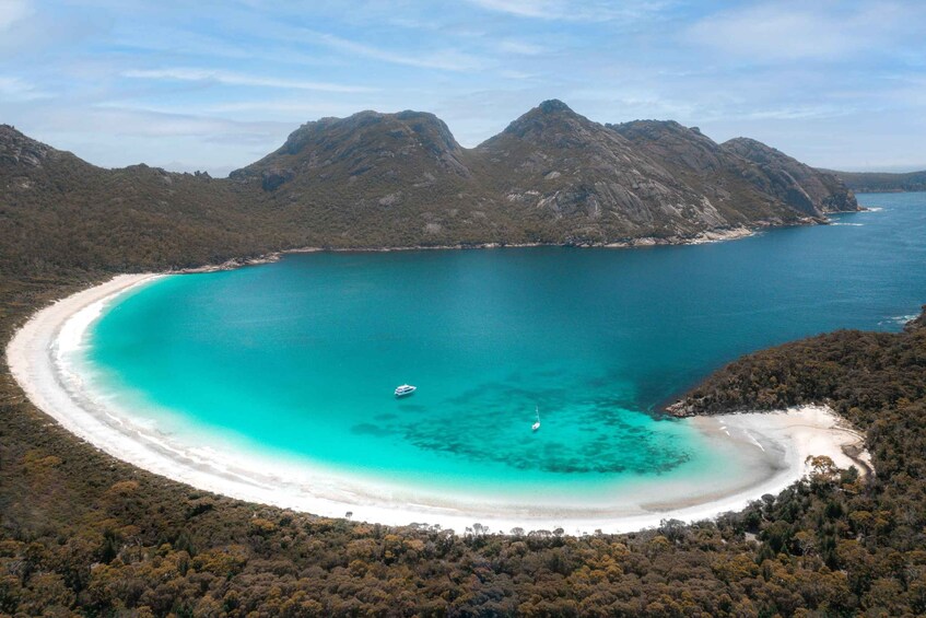 A coastal landscape with a turquoise bay, white sandy beach, and a small boat anchored near the shore. 5