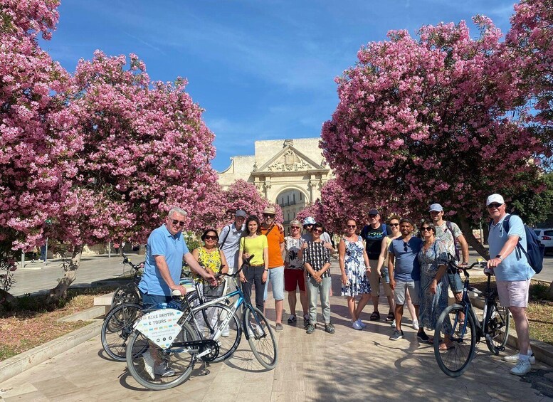 A group of people on bicycles in front of a building with pink flowering trees. 5