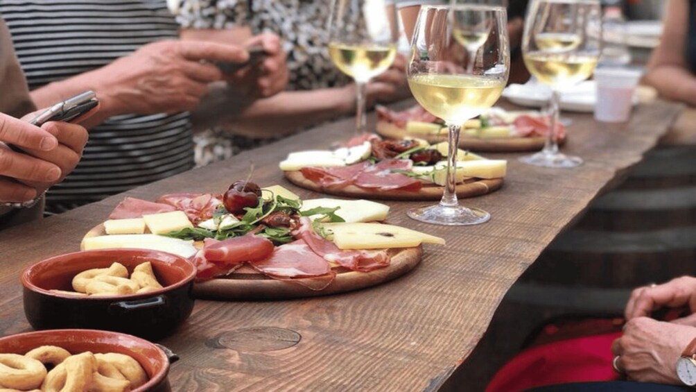 A wooden table with pizzas topped with cheese, prosciutto, and greens, and wine glasses. 2