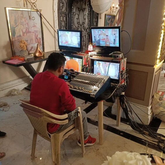 A person sitting at a desk with multiple monitors, a sound mixer, and various cables. 4