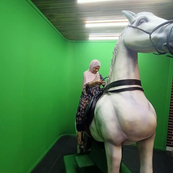 A person riding a stationary horse in a room with green walls and a black floor. 5