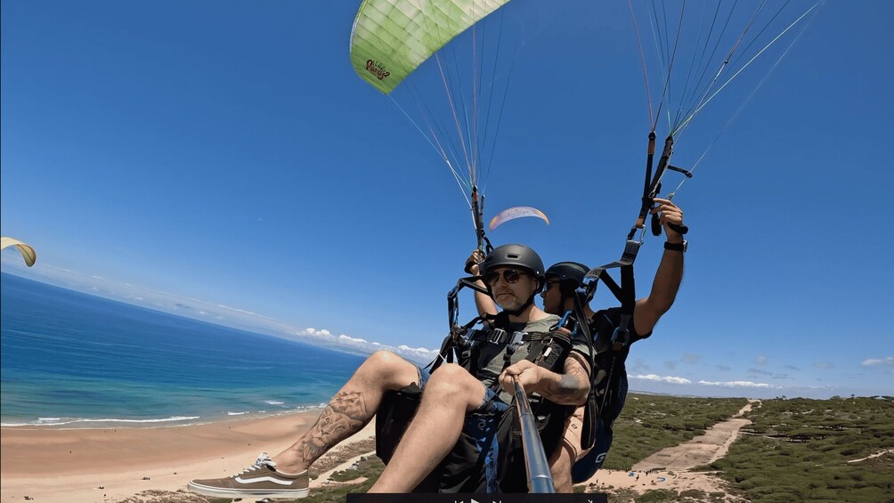 Ein Mensch gleitet mit einem Paragleiter über einen Strand, im Hintergrund strahlend blauer Himmel und das Meer. 5