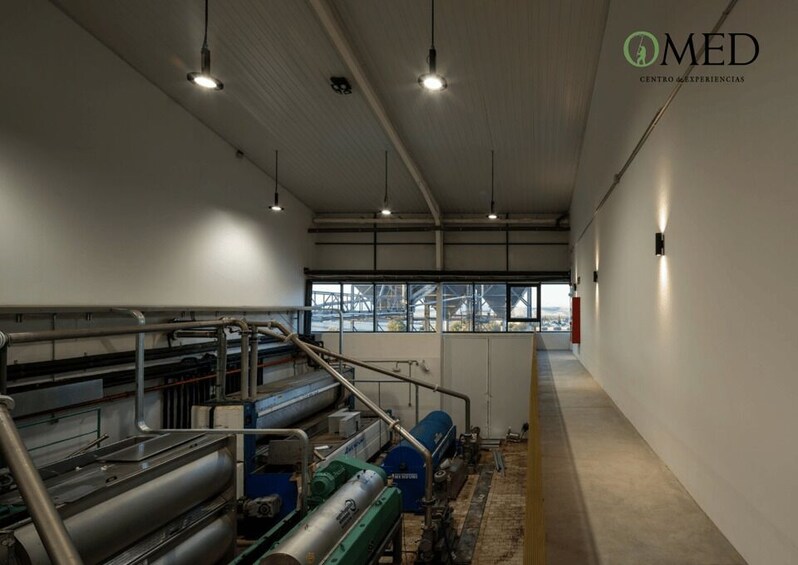 An industrial interior with machinery, a large window, and a logo 'MED Centro de Experiencias' on the wall. 5