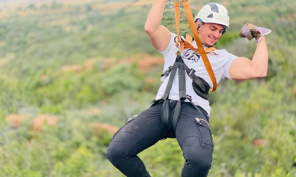 A person in a white t-shirt and black pants with a harness, preparing for a zip-lining activity. 1