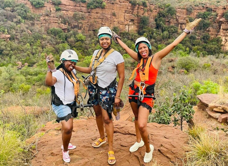 Three people wearing helmets and harnesses, standing on a rocky outcrop with a mountainous background. 4