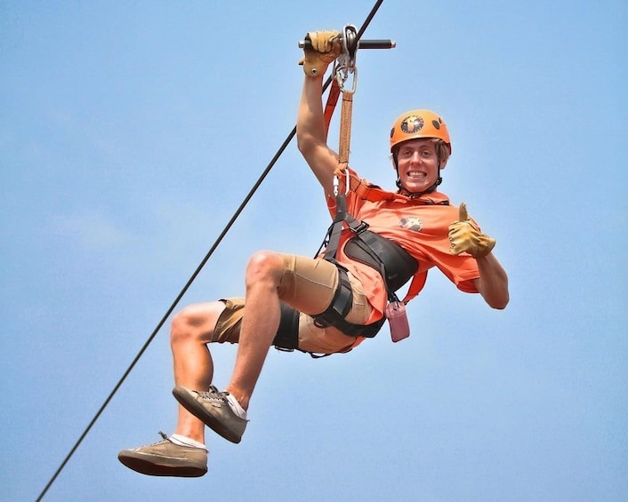 A person ziplining, wearing a helmet and harness, with a clear sky in the background. 2