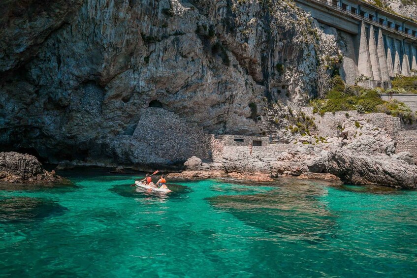 Un mar turquesa cristalino con una costa rocosa, un muro de piedra y un puente. 4