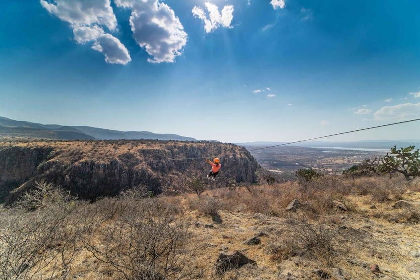 A person bungee jumping from a high cliff with a clear view of the landscape and mountains in the background. 1