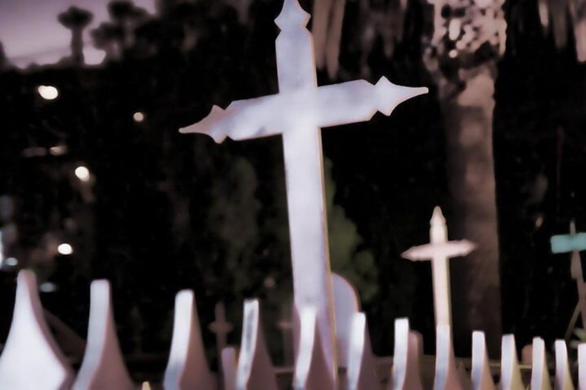 Une croix blanche à sommet pointu, entourée d’autres croix sur un fond sombre. 2