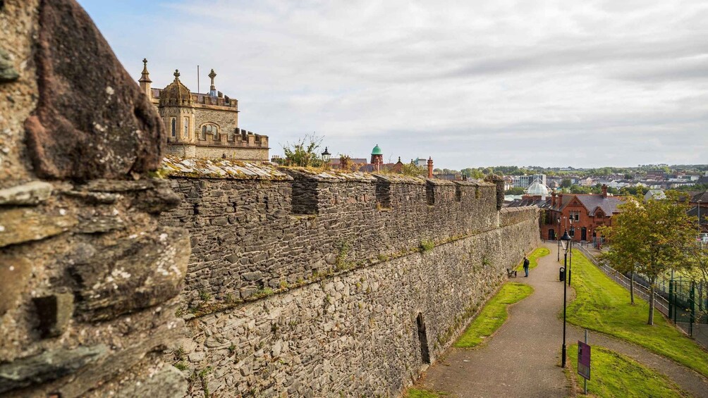 A stone wall with a castle on top, a pathway, and a distant town. 3