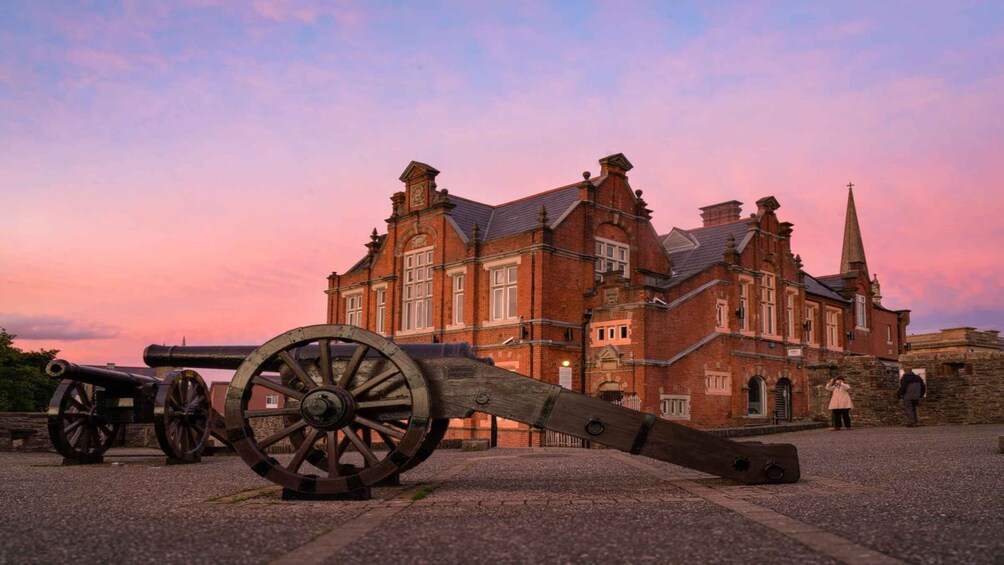 A historic building with a clock tower and a large cannon in front. 4