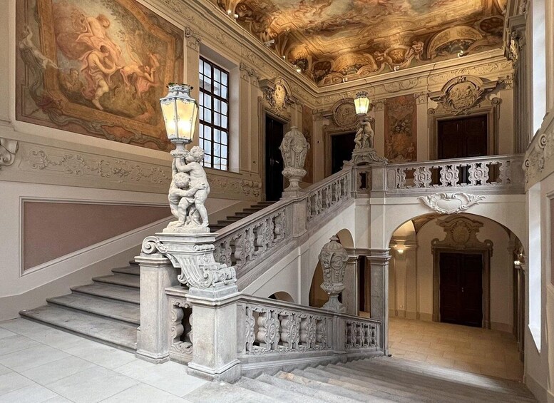 An ornate staircase with intricate carvings and a mural on the ceiling. 1