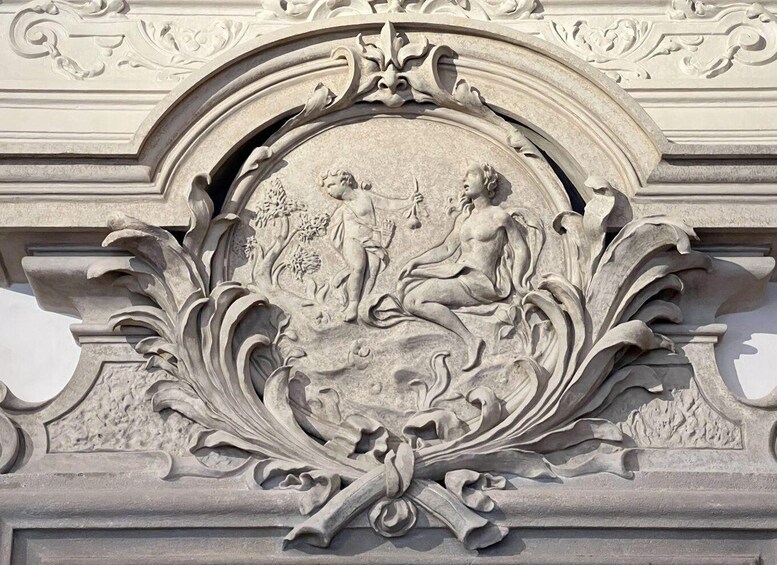 A detailed stone relief sculpture with two figures, one standing and one seated, surrounded by ornate foliage and floral motifs. 2