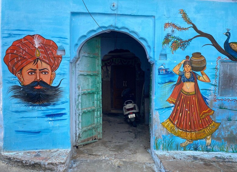 Un mural con un pavo real, una mujer cargando una olla y un hombre con turbante sobre un muro azul. 4
