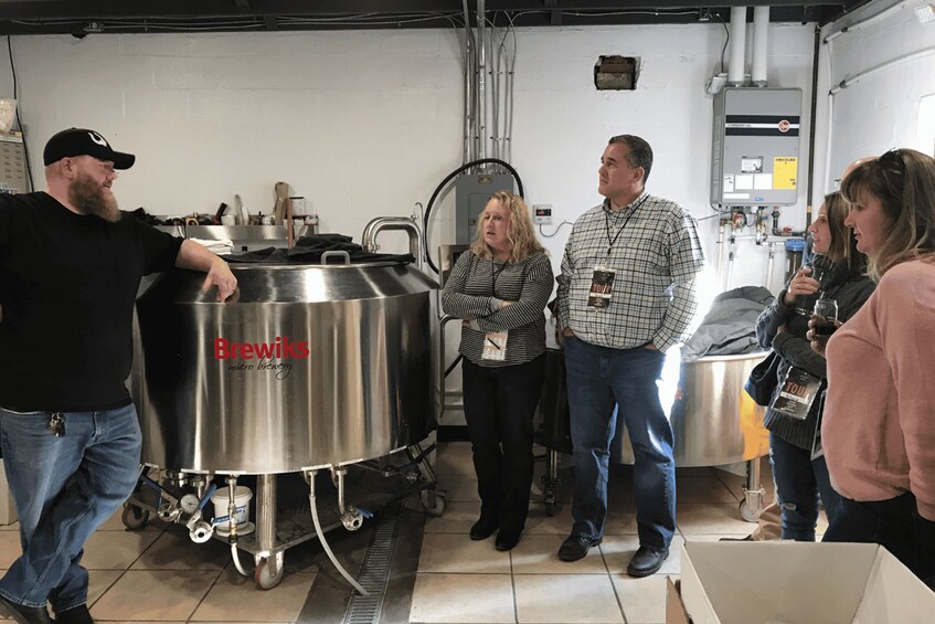 A group of people in a brewery setting with stainless steel brewing equipment. 5