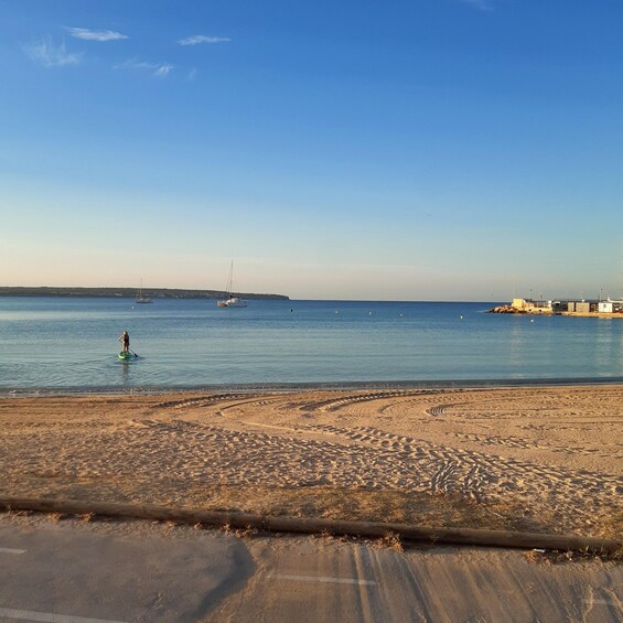 Een strand met een persoon die op een paddleboard staat, een rustige zee en verre boten. 2