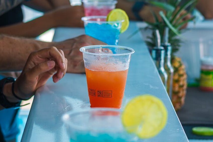 A bar setting with a person holding a plastic cup with an orange beverage, a pineapple, and a lime wedge on the counter. 2