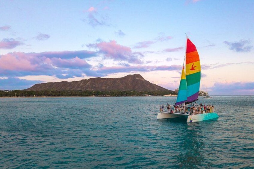 A sailboat with a rainbow sail on a calm sea, with a mountain in the background. 2