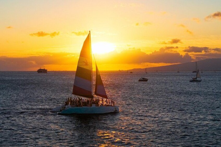 A sailboat with passengers at sunset, calm sea, and other boats in the distance. 5