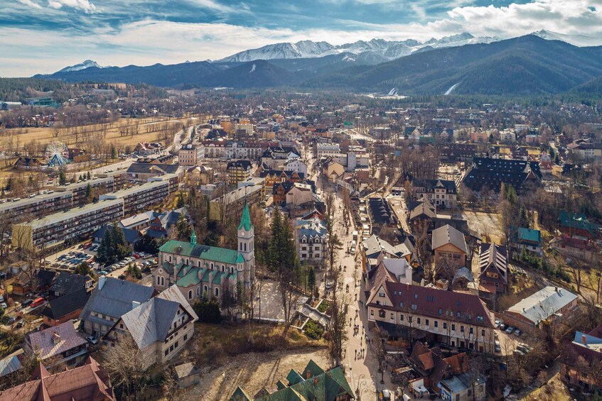 Une ville qui se distingue par son église imposante, une grande roue et des montagnes en arrière-plan. 2