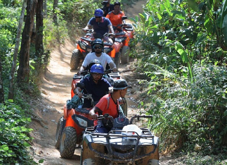 Four people riding ATVs on a dirt path surrounded by greenery. 1