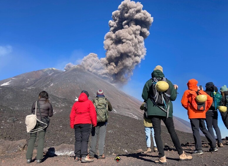 A group of people observing a volcanic eruption with smoke and ash rising from the mountain. 1