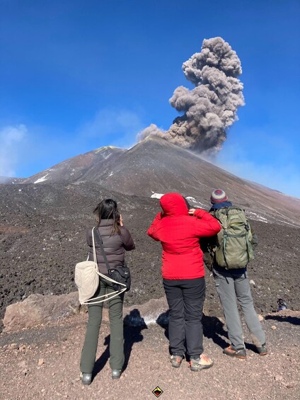 Three people observing a volcano with smoke and ash plumes. 4