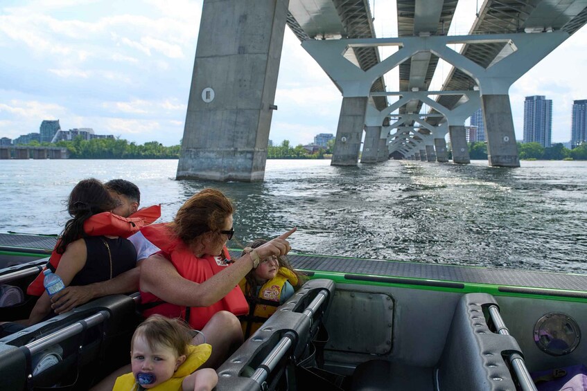 A boat with passengers wearing life jackets, a bridge in the background, and a city skyline across the water. 2