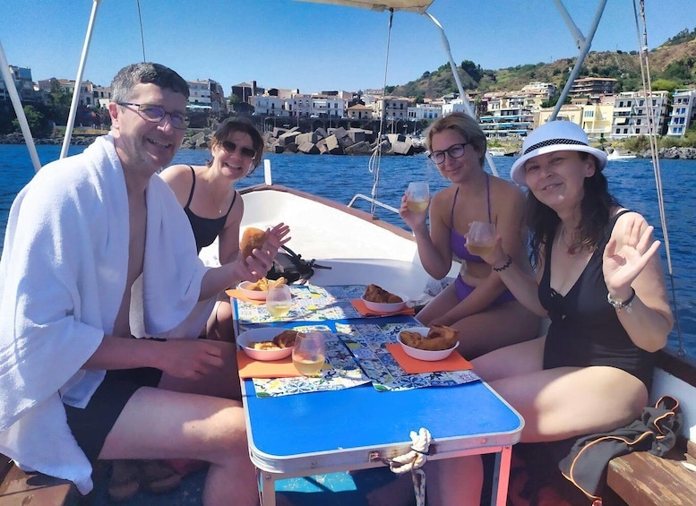 Un gruppo di persone su una barca, con un tavolo apparecchiato per un pasto, circondate dall'acqua e da edifici sullo sfondo. 3