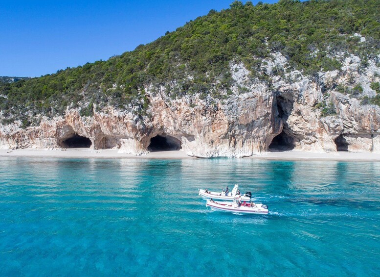 A coastal scene with clear turquoise waters, a rocky cliff with caves, and a boat with passengers. 3