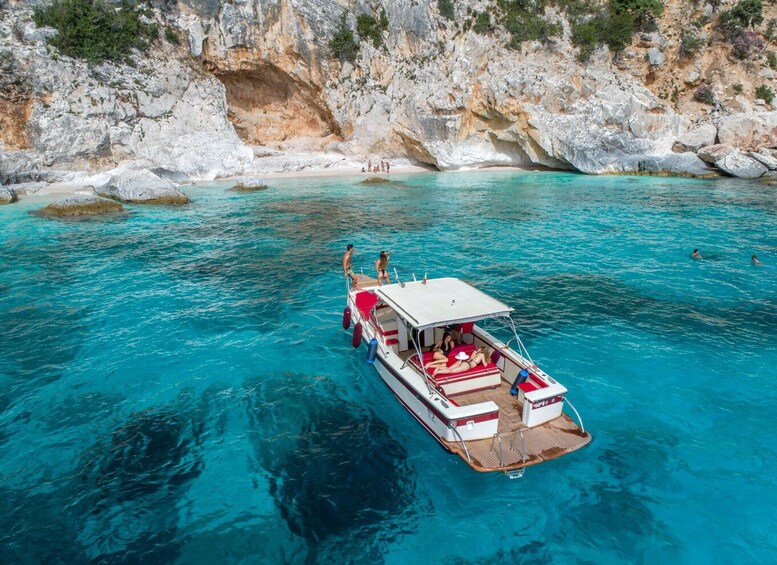 A boat with passengers on a clear turquoise sea, rocky cliffs in the background. 1