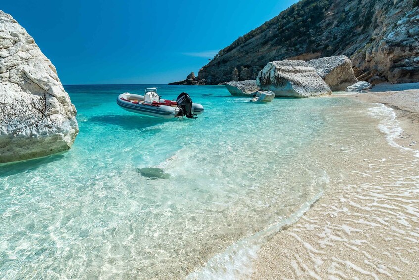 A clear turquoise sea, a sandy beach, and a motorboat anchored near large white rocks. 2