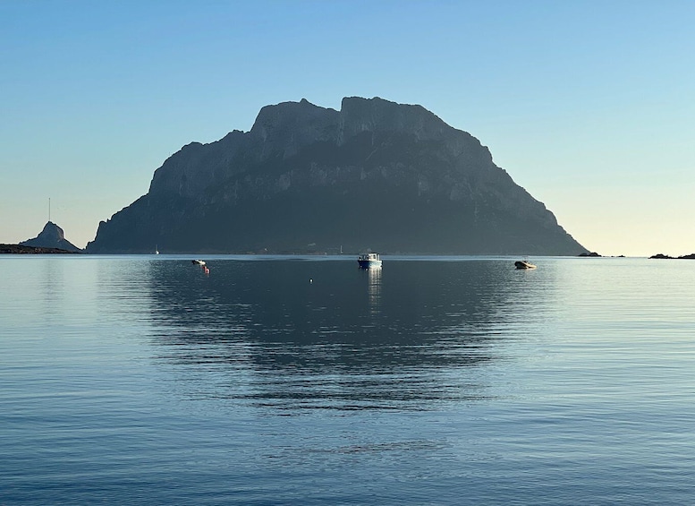 A calm sea with a large rock formation in the distance and several boats. 4