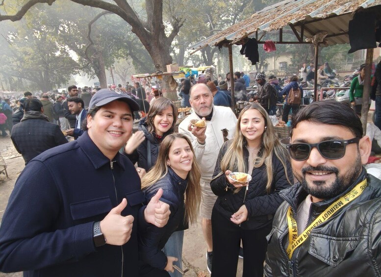 A group of people at an outdoor market with various stalls and trees in the background. 3