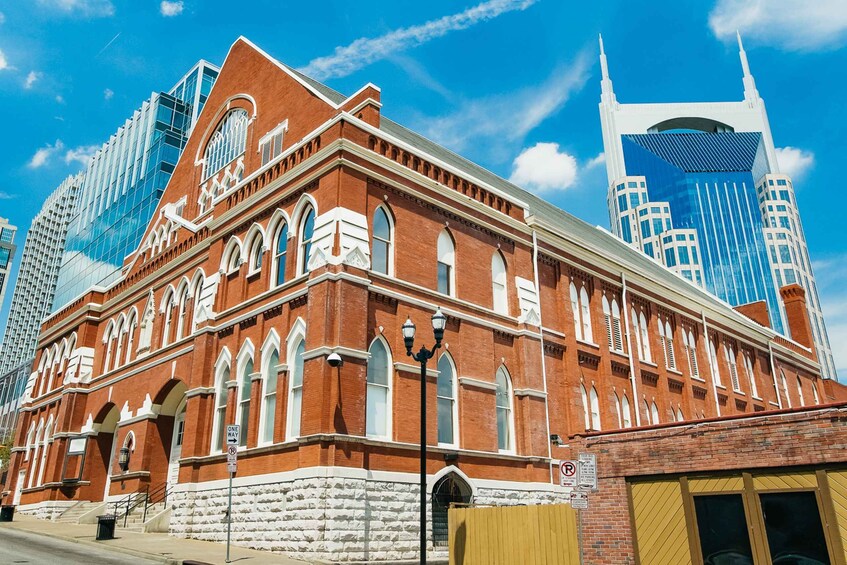 A historic red brick building with arched windows and a clock tower, surrounded by modern skyscrapers. 1