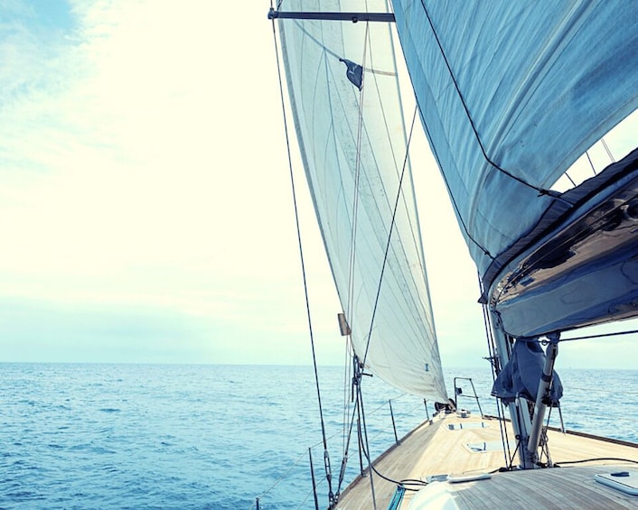 A sailboat on the ocean with sails unfurled, a wooden deck, and a clear sky. 5