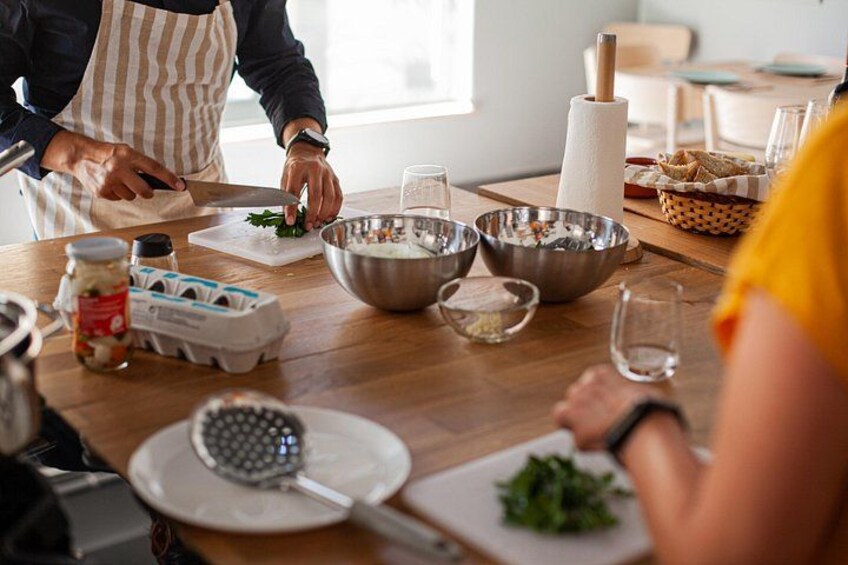Una cocina con una persona picando verduras, una tabla de cortar, cuencos, un rodillo y una cesta de pan. 5